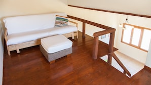 A wooden floor, a white sofa with a striped pillow, and a wooden railing. - Karthea VI (Kea)