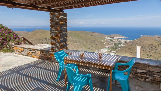 A patio with a stone table and turquoise chairs, overlooking a coastal landscape. - Karthea VI (Kea)