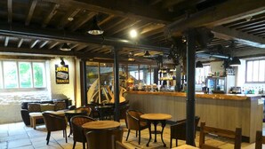 A cozy restaurant interior with wooden tables and chairs, a bar area, and a large window with a view of trees. - (101)Beautiful Apartment in Landmark Cotswold Grade II Listed Georgian House -  (Nailsworth)