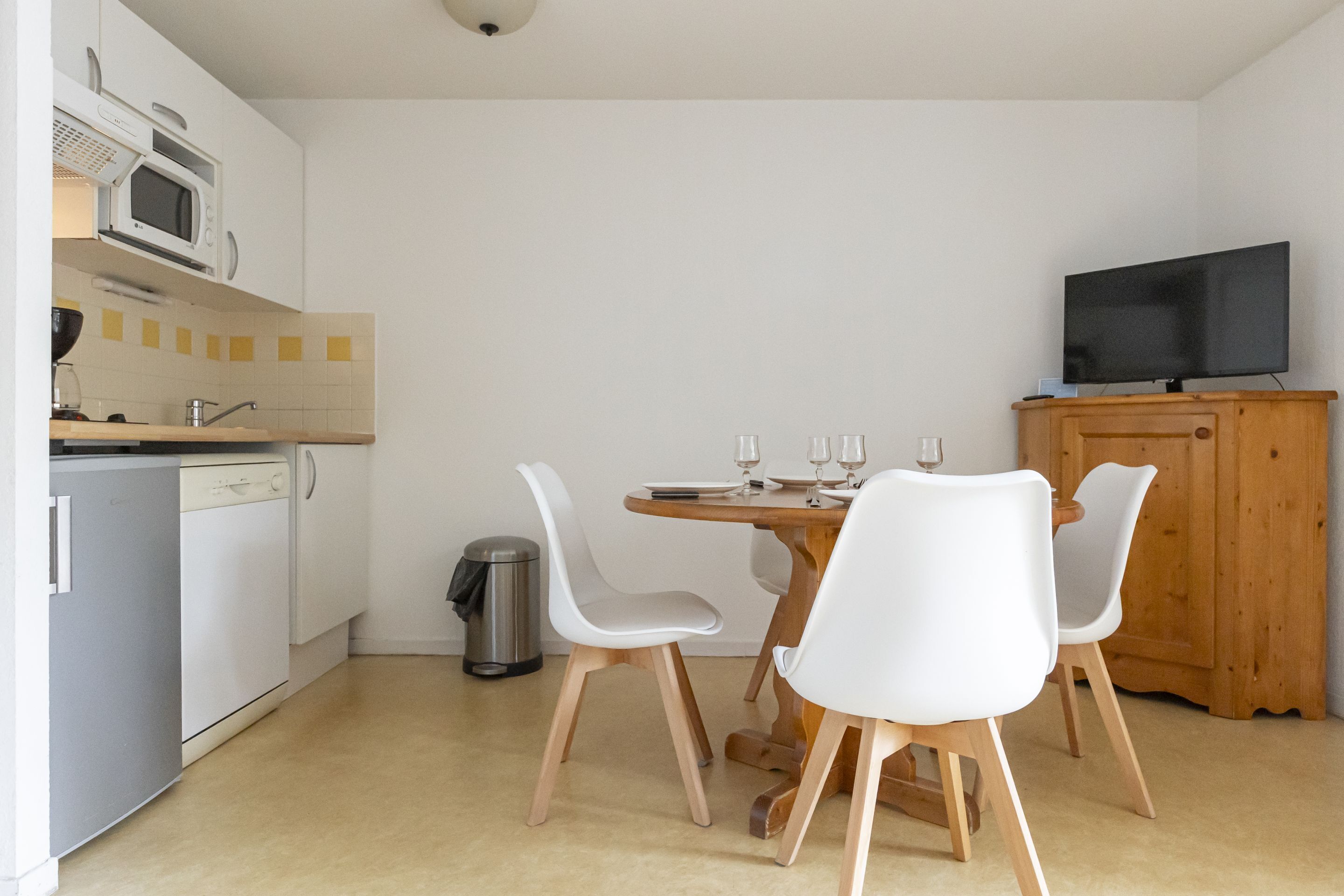 Eine kleine Küche mit Mikrowelle, Spüle und Geschirrspüler, ein Essbereich mit Tisch und Stühlen sowie ein Fernseher auf einem Holzkasten.