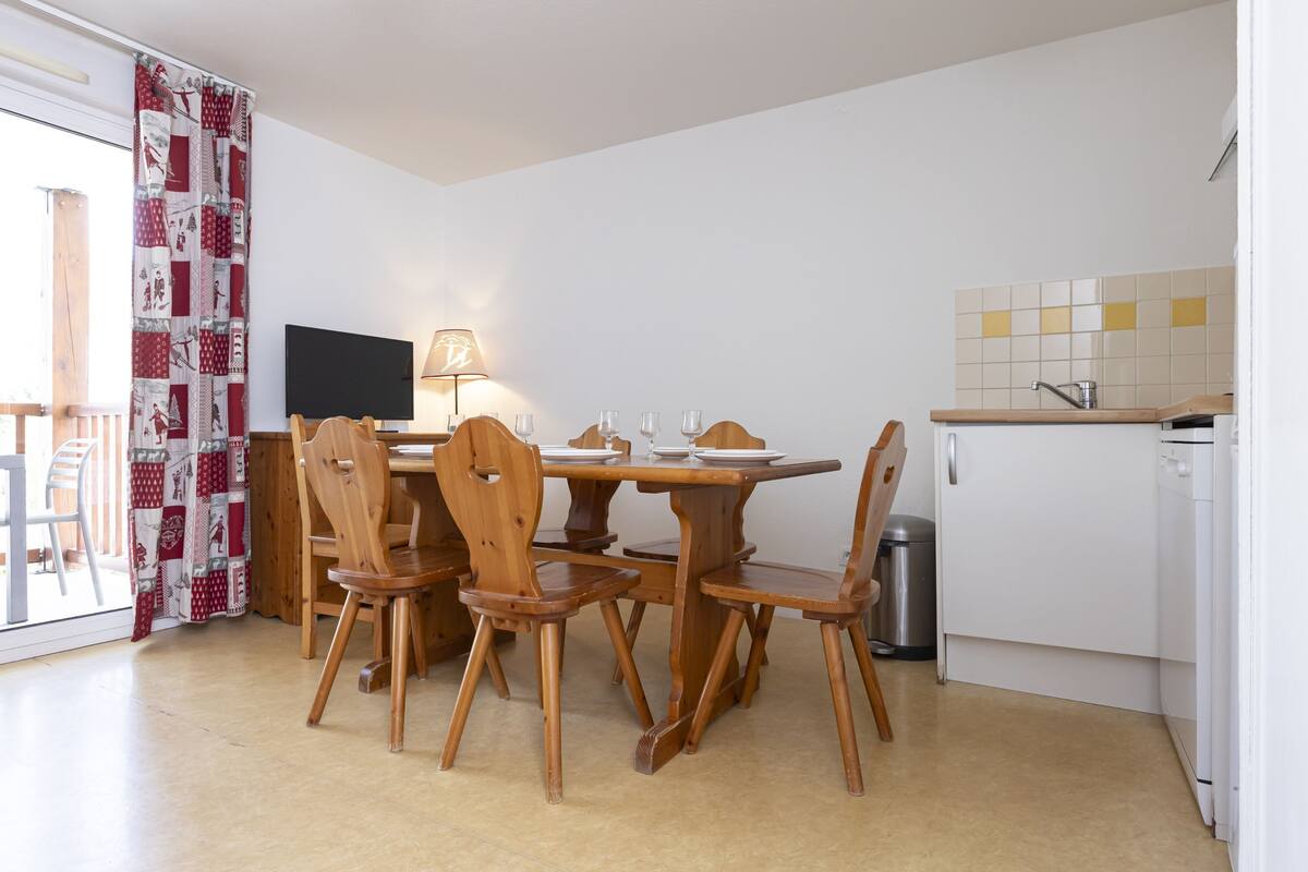 A dining area with a wooden table and chairs, a TV, and a kitchen area with a sink and cabinets.