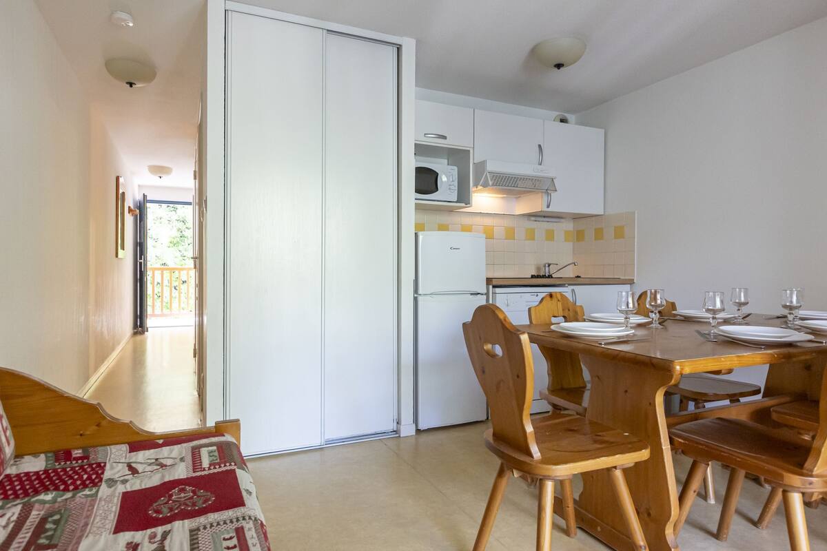 A compact kitchen with white cabinets, a microwave, and a refrigerator. There is a dining table set with plates and glasses.