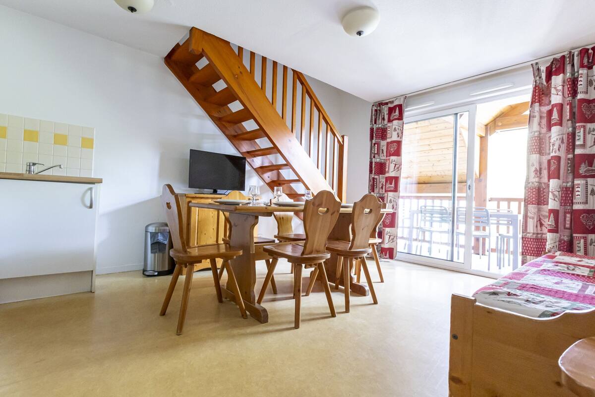 A dining area with a wooden table and chairs, a television, and a staircase leading to a balcony.