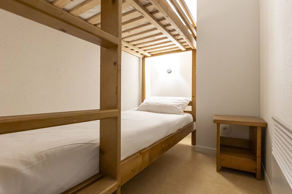 A bunk bed room with a wooden headboard, a small bedside table, and a white wall.