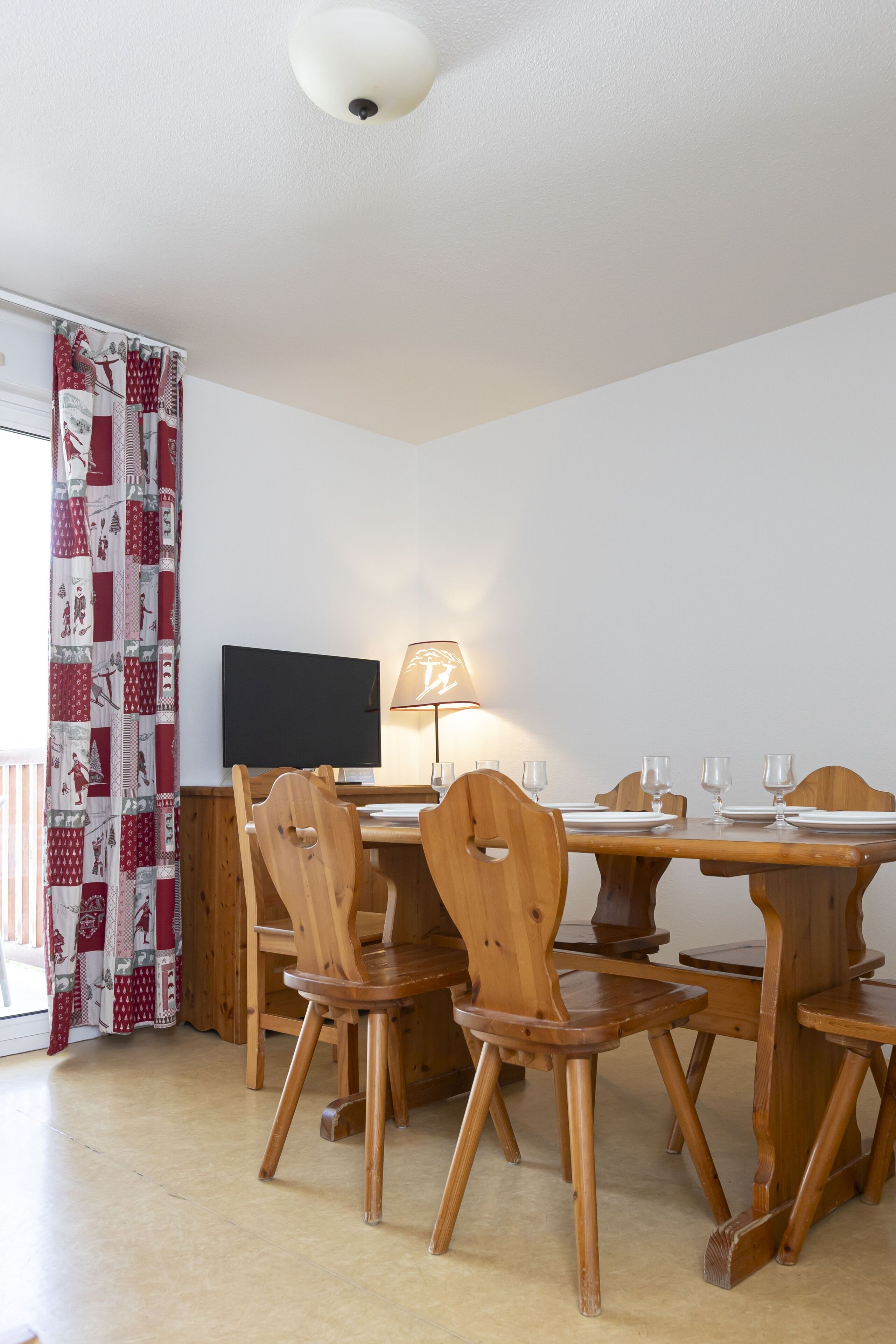 A dining area with a wooden table and chairs, a flat-screen TV, and a lamp.