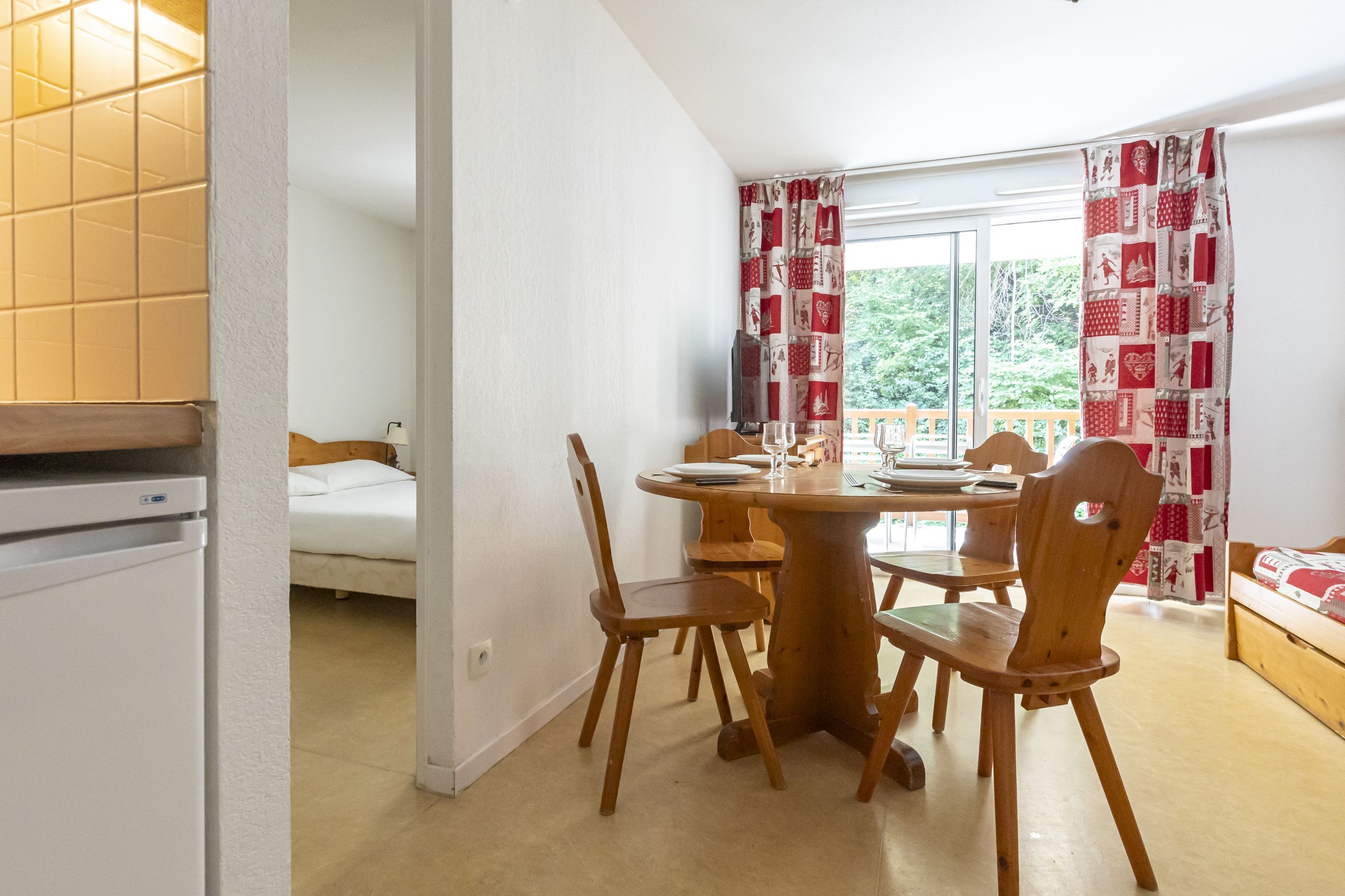 Una habitación pequeña con una mesa de comedor y sillas, una cama y una ventana con cortinas.