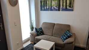 A living room with a sofa, two patterned cushions, a white coffee table, and a wall-mounted clock. - Business Apartments Ratingen 5 (Ratingen)