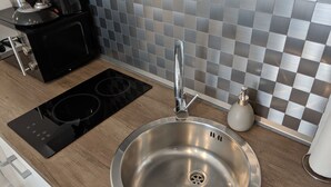 A modern kitchen with a stainless steel sink, black induction cooktop, and a tiled backsplash. - Business Apartments Ratingen 5 (Ratingen)