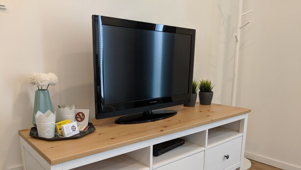 A flat-screen TV on a wooden TV stand with a white drawer unit below. - Business Apartments Ratingen 5 (Ratingen)