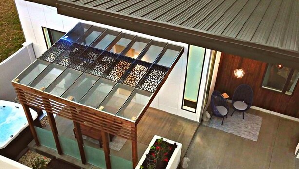 Una casa moderna con un patio envuelto en vidrio, un jacuzzi y un pequeño jardín.
