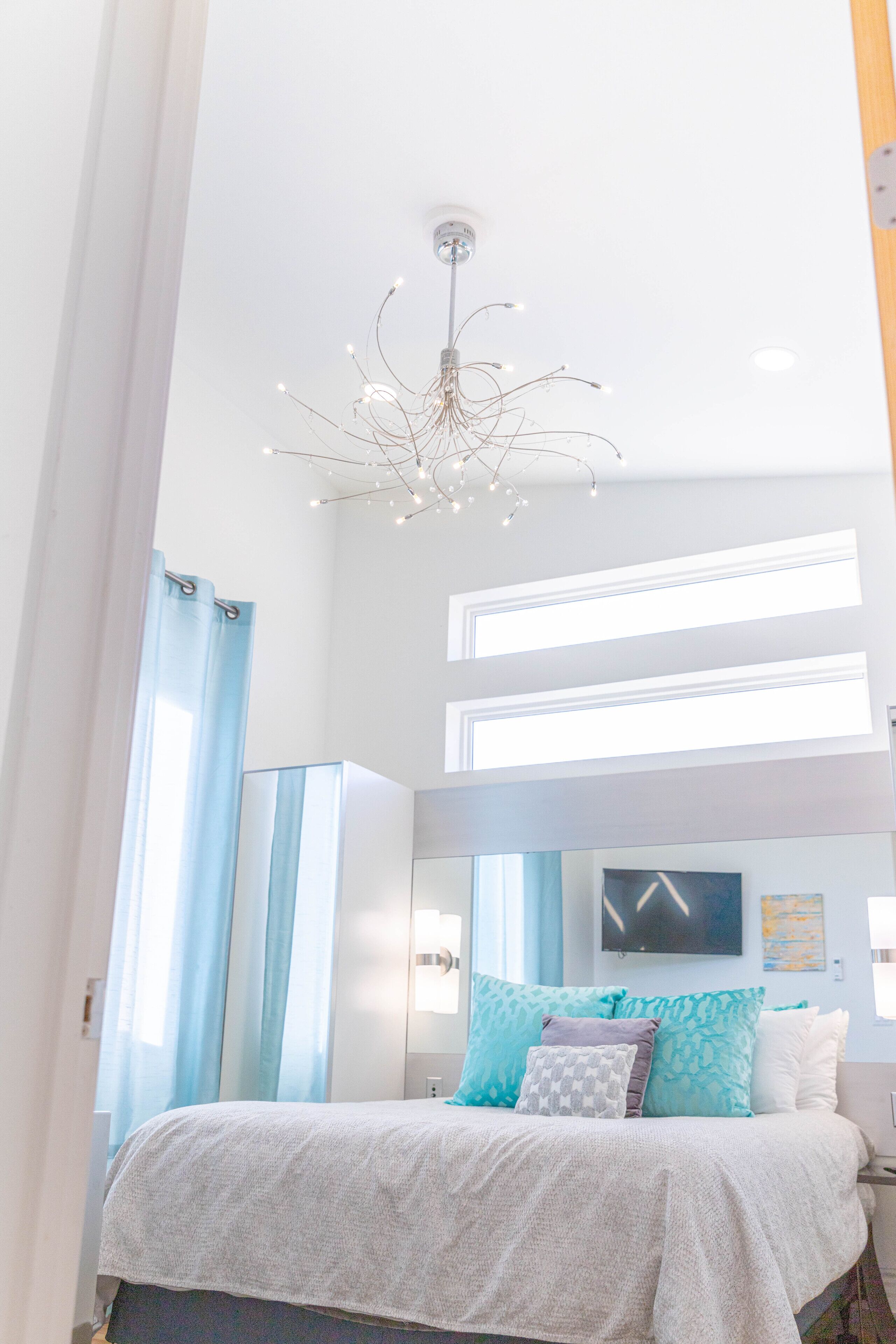 A modern bedroom with a bed, a chandelier, and a large window.