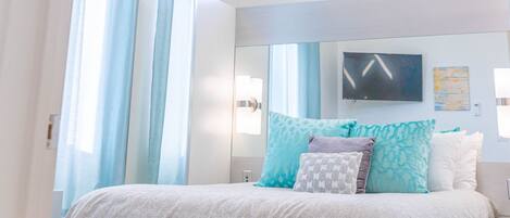 A modern bedroom with a bed, a chandelier, and a large window.