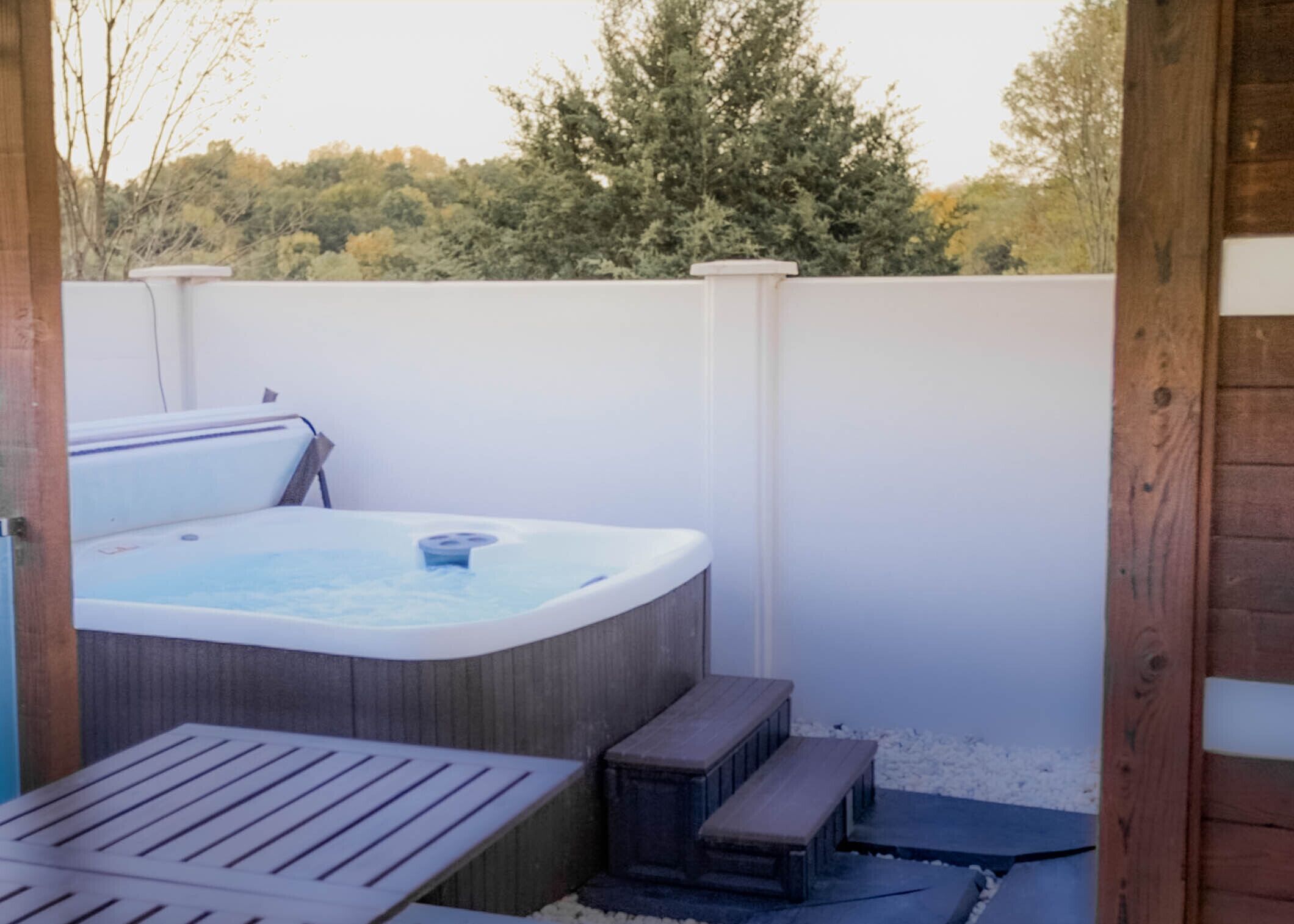 A hot tub in a covered outdoor area with a wooden bench and steps leading up to it.
