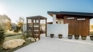 Una casa moderna con una pérgola de madera, plantas en macetas y un camino de concreto.