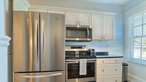 A modern kitchen with stainless steel appliances, white cabinetry, and a window with blinds. - Private Parking and Unbeatable Location on Liberty Street by Lucky Savannah (Savannah)