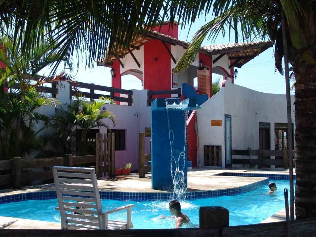 Uma piscina com escorregador, palmeiras e um edifício com fachada vermelha e branca.