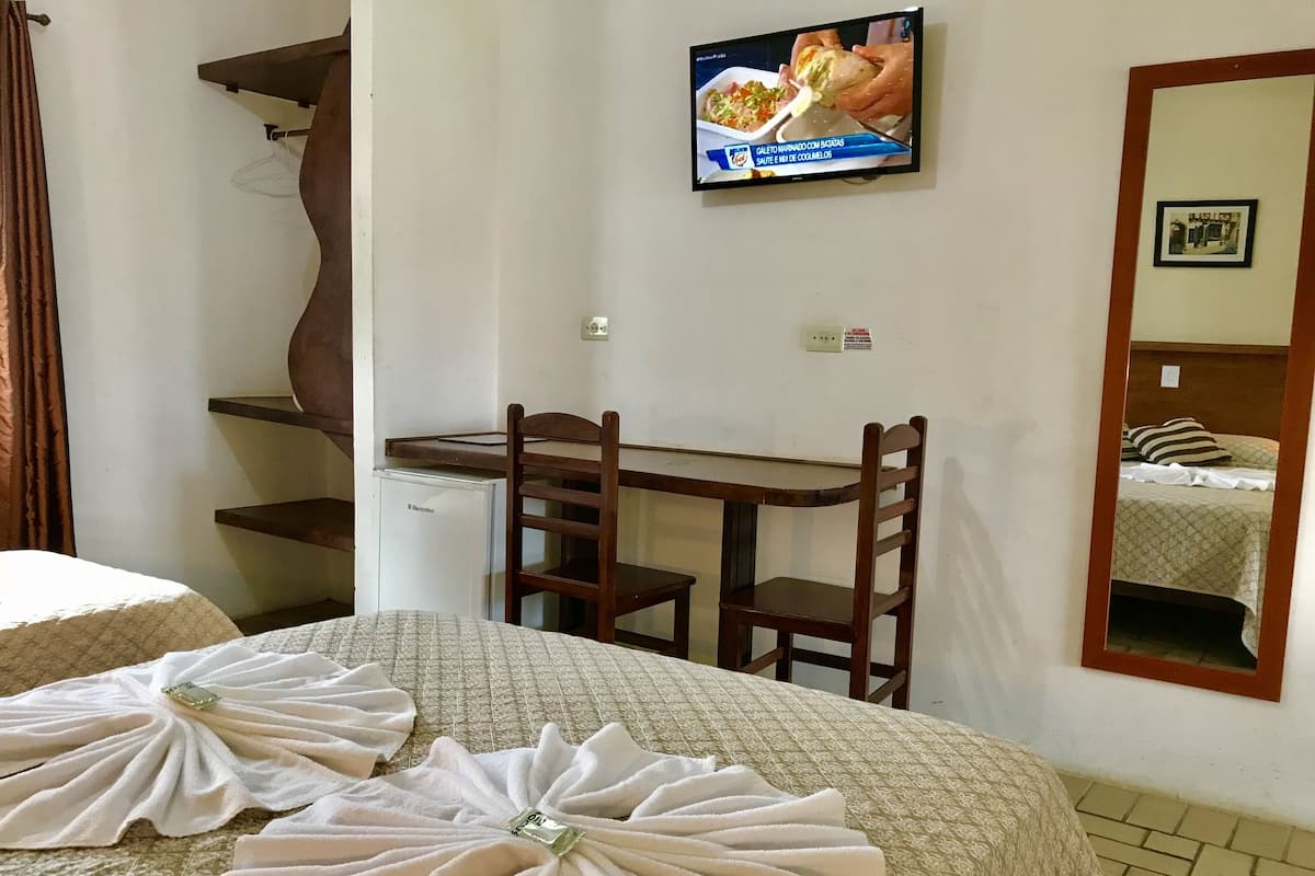 Ett hotellrum med en säng, ett skrivbord, en stol, en tv och en spegel.