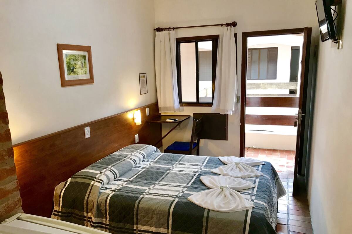 Ett hotellrum med en säng, ett skrivbord, en stol, en tv och ett fönster med gardiner.