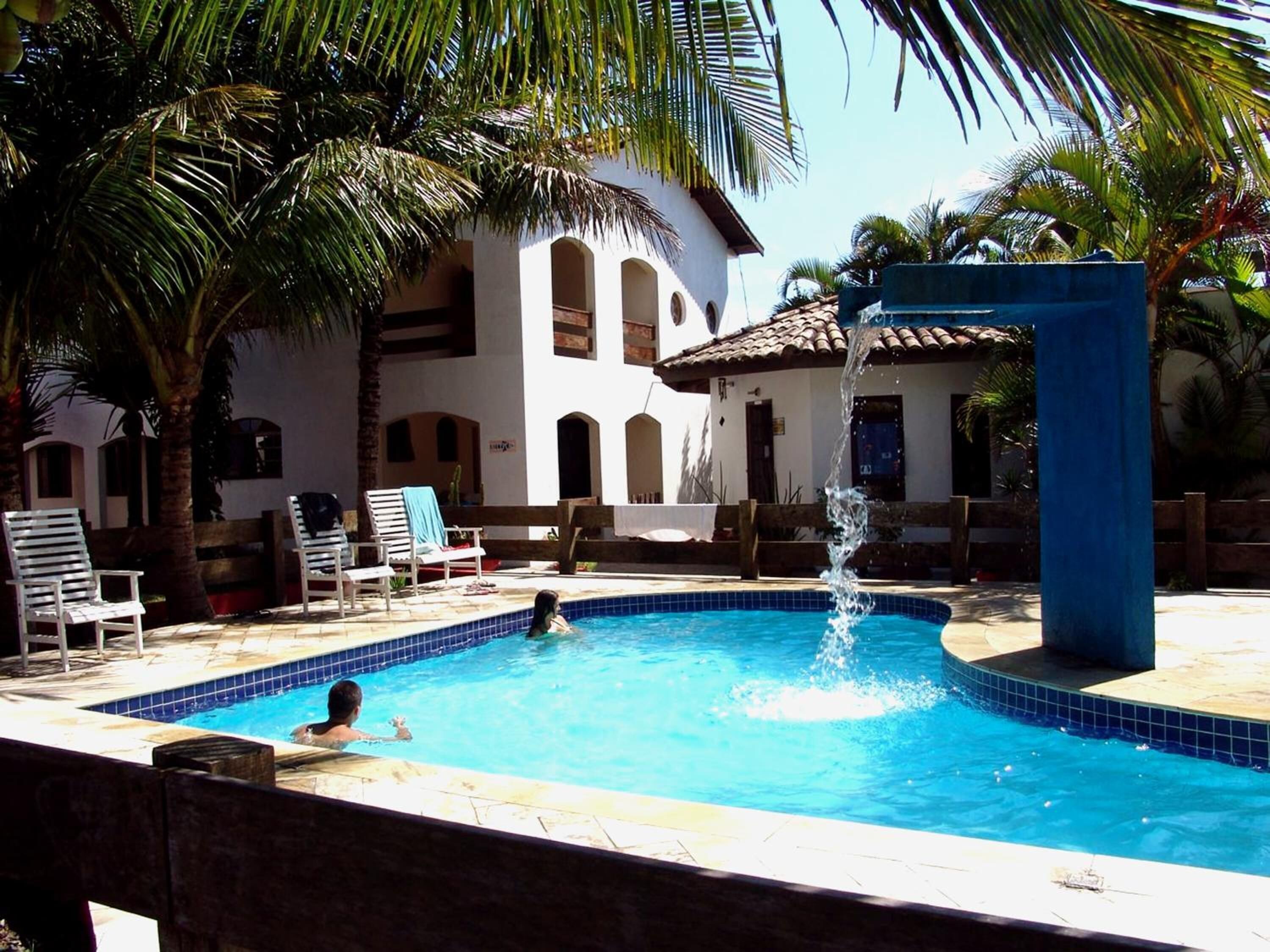 A swimming pool with a water fountain, surrounded by palm trees and lounge chairs.