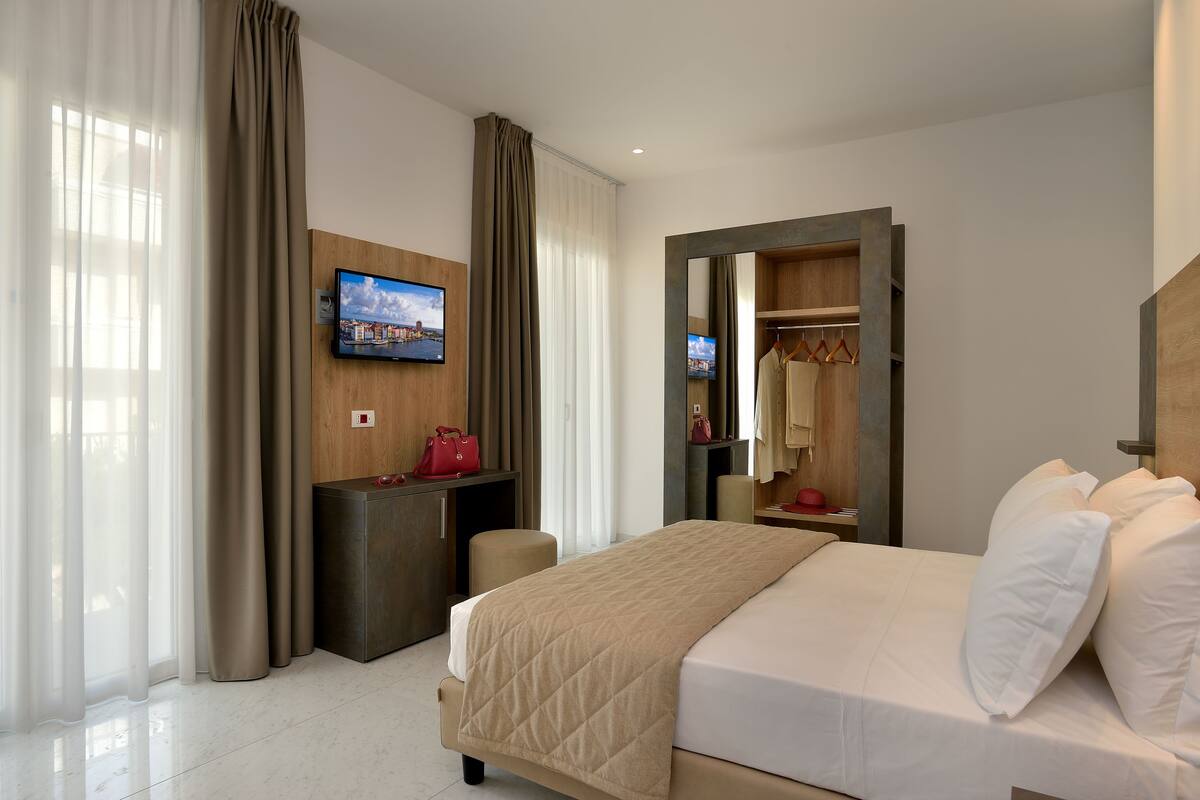 A hotel room with a bed, a desk, a TV, a wardrobe, and a mirror.