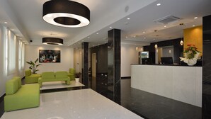 A modern lobby with a reception desk, green seating area, and a large mirror. - Hotel Ducale (Rimini)