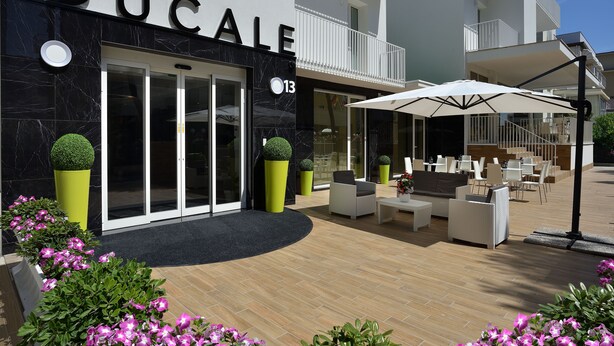 A hotel exterior with a black facade, a glass entrance, outdoor seating, and potted plants. - Hotel Ducale (Rimini)