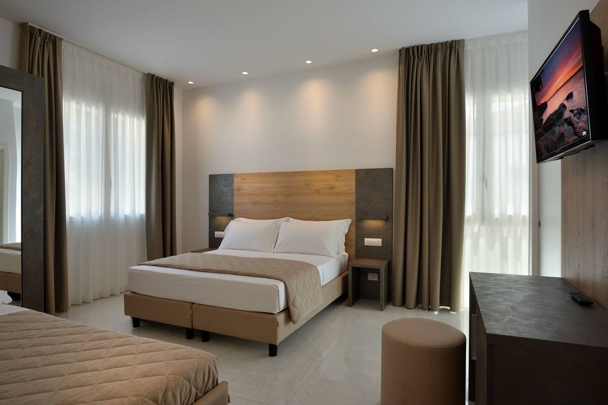A modern hotel room with a large bed, bedside tables, a TV, and a desk.
