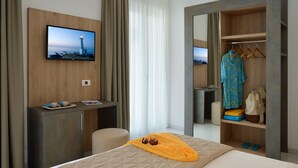 A hotel room with a bed, a desk with a TV, a wardrobe, and a view of the sea. - Hotel Ducale (Rimini)