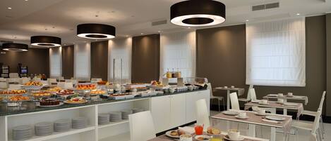 A modern breakfast area with a buffet, white chairs, and a long table set for dining.