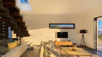 A modern living room with a sofa, coffee table, TV, and a staircase.