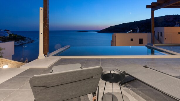 Ein Poolbereich mit Meerblick, eine Liege und ein kleiner Tisch.