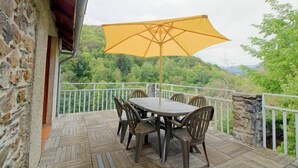 A wooden deck with a table and chairs, a yellow umbrella, and a stone wall.