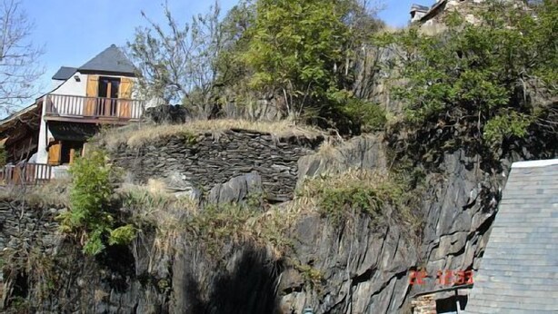 A house built into a rocky hillside with a balcony overlooking the landscape.