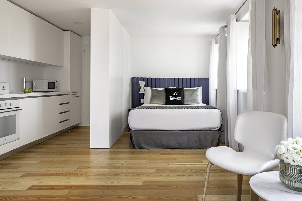 Una habitación de hotel moderna con kitchenette, una cama con cabecera y una zona de estar con mesa.