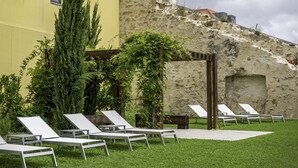 Un patio con sillones blancos, un muro de piedra y un edificio amarillo.
