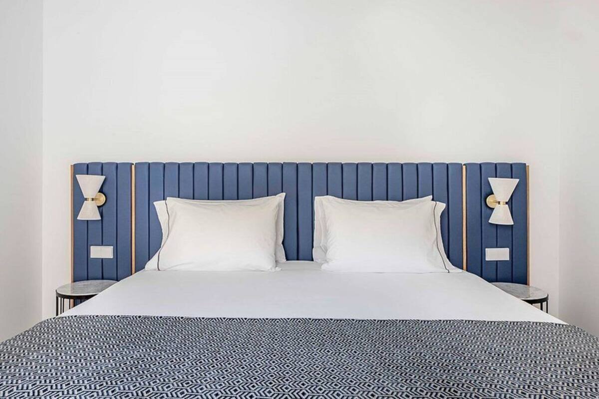 Una cama con cabecera azul, dos almohadas blancas y una colcha estampada.