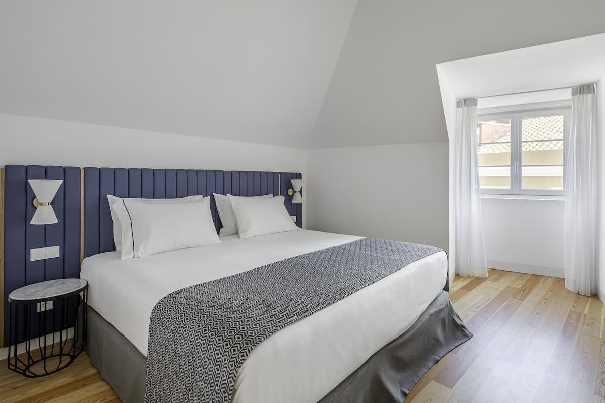 Un dormitorio ordenado con cama, mesitas de noche y una ventana con cortinas.