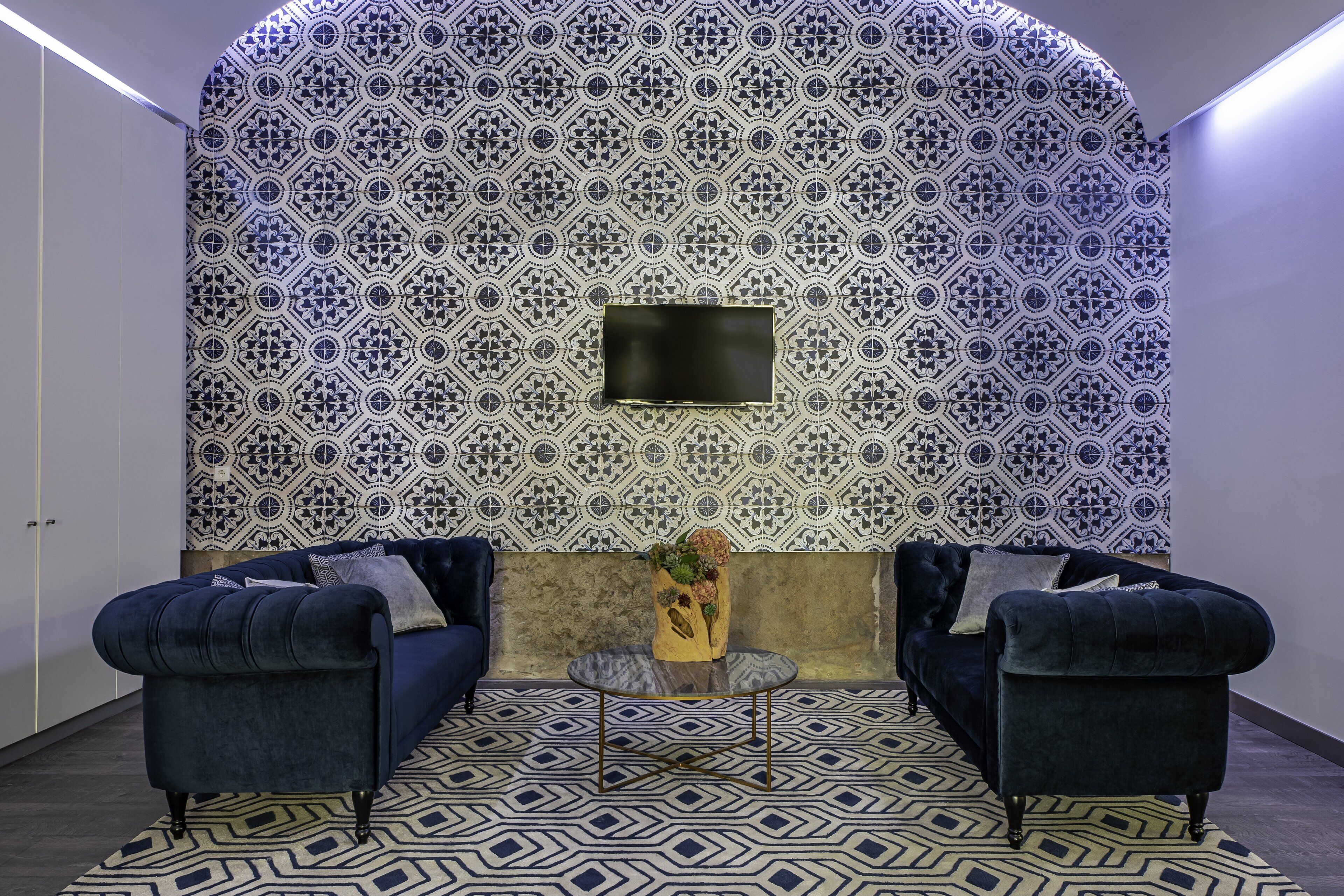 Una habitación con pared estampada, dos sofás, una mesita y un televisor de pantalla plana montado en la pared.