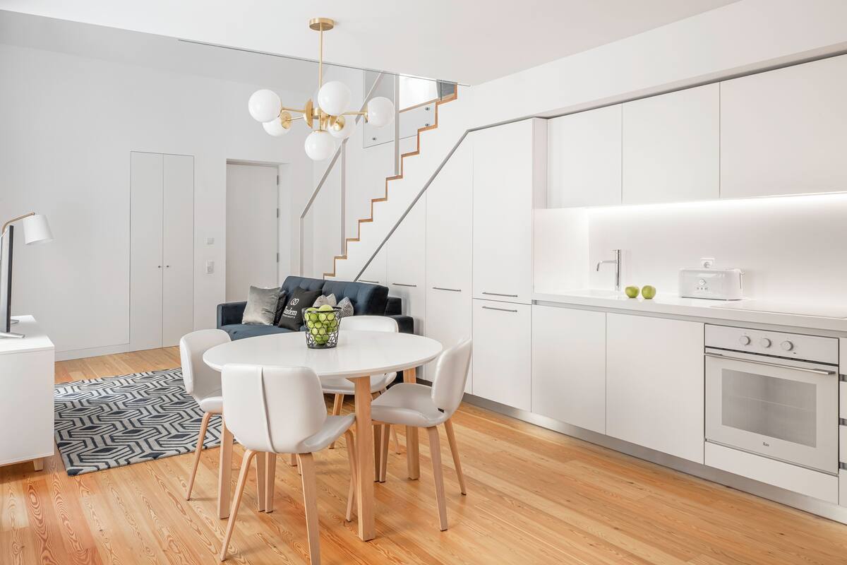 Una cocina moderna con armarios blancos, horno empotrado y comedor con una mesa y sillas redondas.
