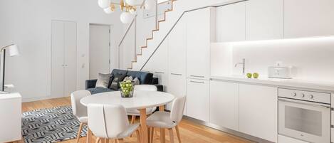 A modern kitchen with white cabinets, a built-in oven, and a dining area with a round table and chairs.