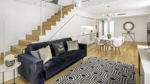 Una sala de estar moderna con un sofá azul oscuro, un tapete con estampado geométrico y una escalera que sube a un nivel superior.