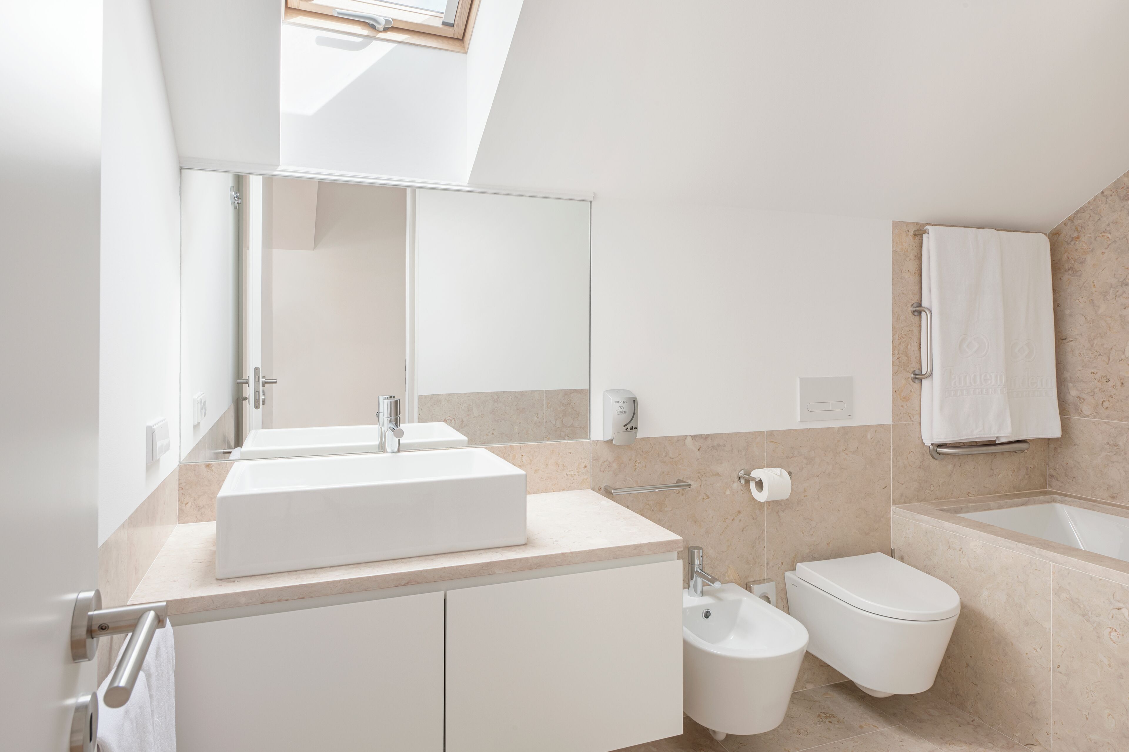 A modern bathroom with a large mirror, a double sink, a toilet, and a bathtub.