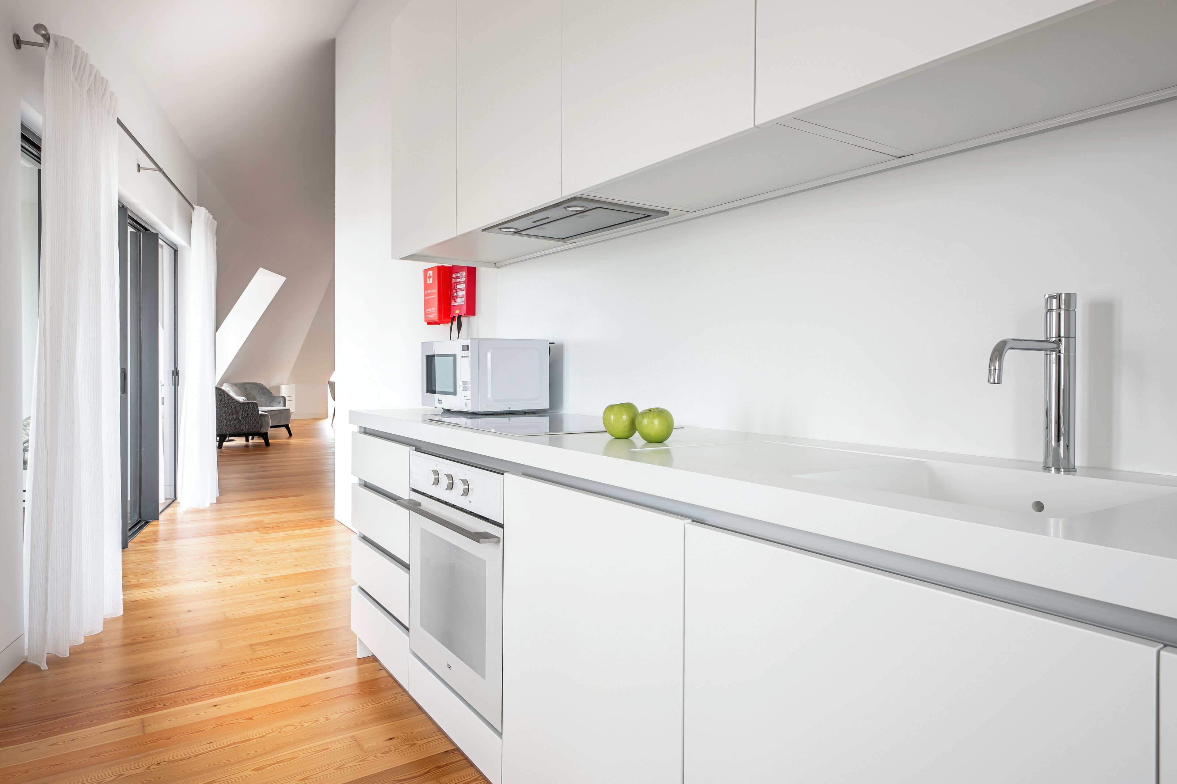 A modern kitchen with white cabinetry, a stainless steel sink, and a microwave. There are two green apples on the counter.