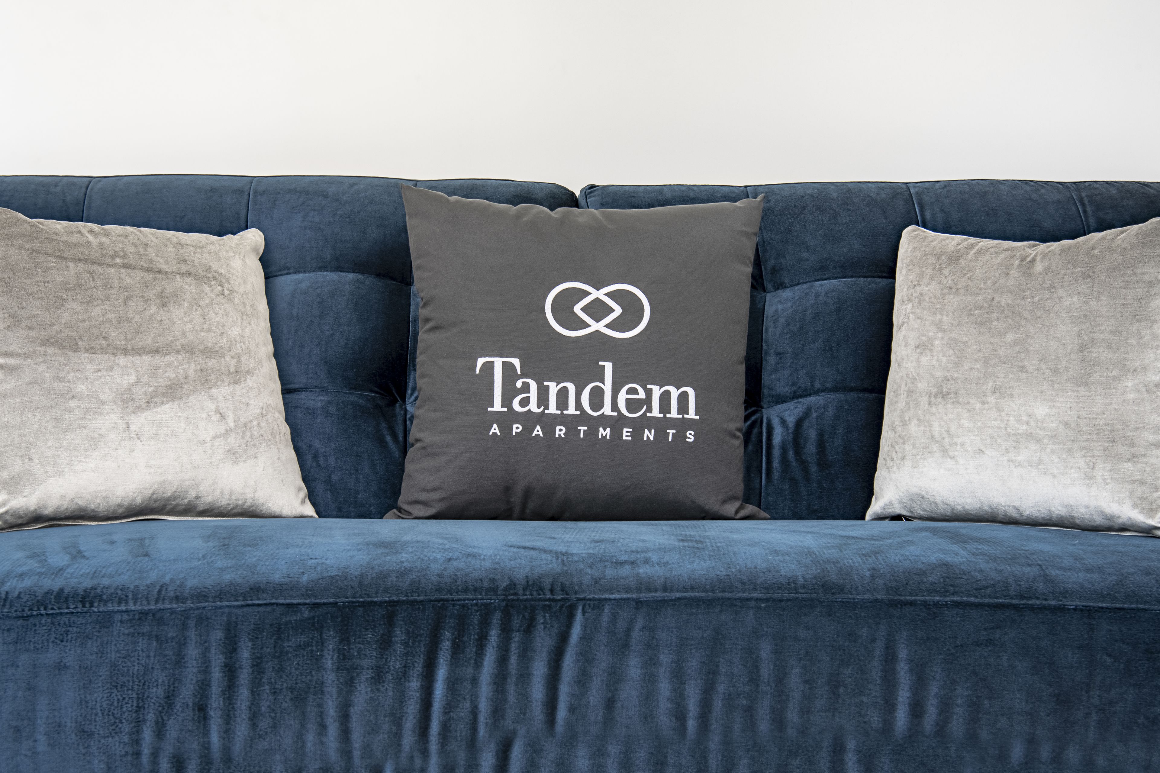 A blue sofa with three pillows, one with "Tandem Apartments" text.