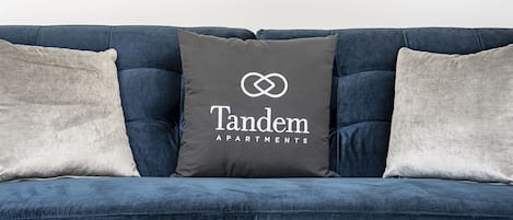 A blue sofa with three pillows, one with "Tandem Apartments" text.