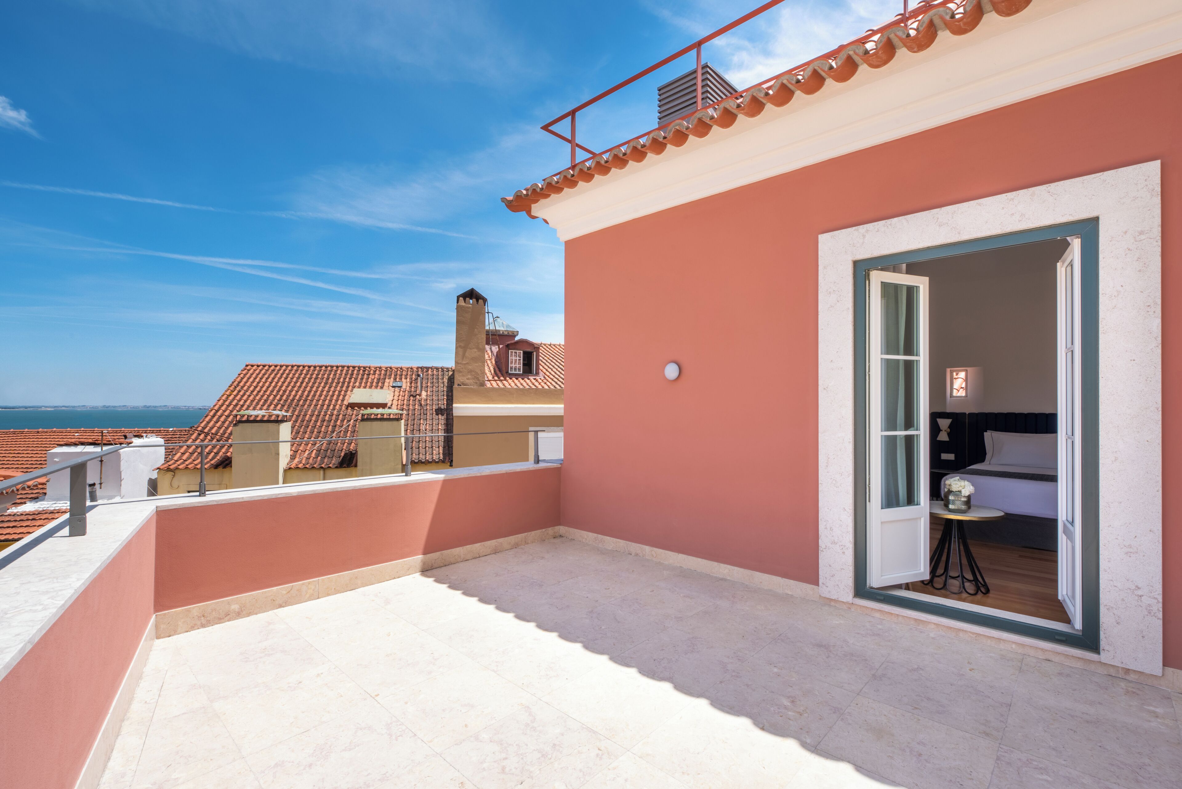 Eine Dachterrasse mit Meerblick, ein Balkon mit Geländer und eine Tür zu einem Zimmer mit einem Bett und einem kleinen Tisch.