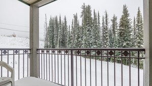 En balkon med gelænder i metal, der udover et sneklædt landskab med træer.