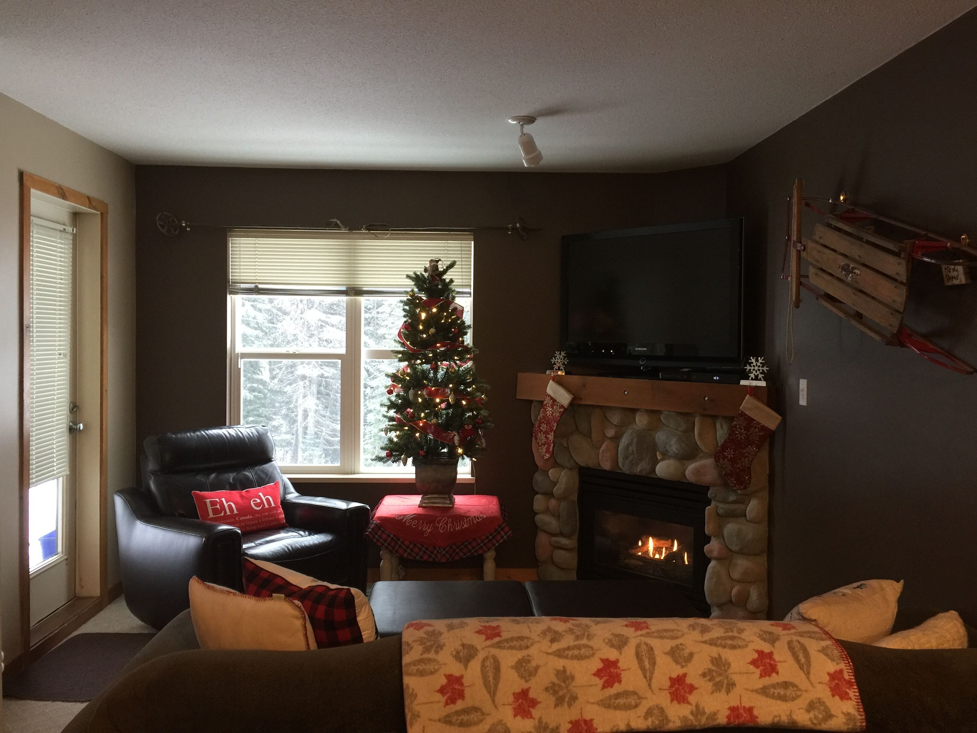 A cozy living room with a fireplace, a Christmas tree, a television, and comfortable seating.