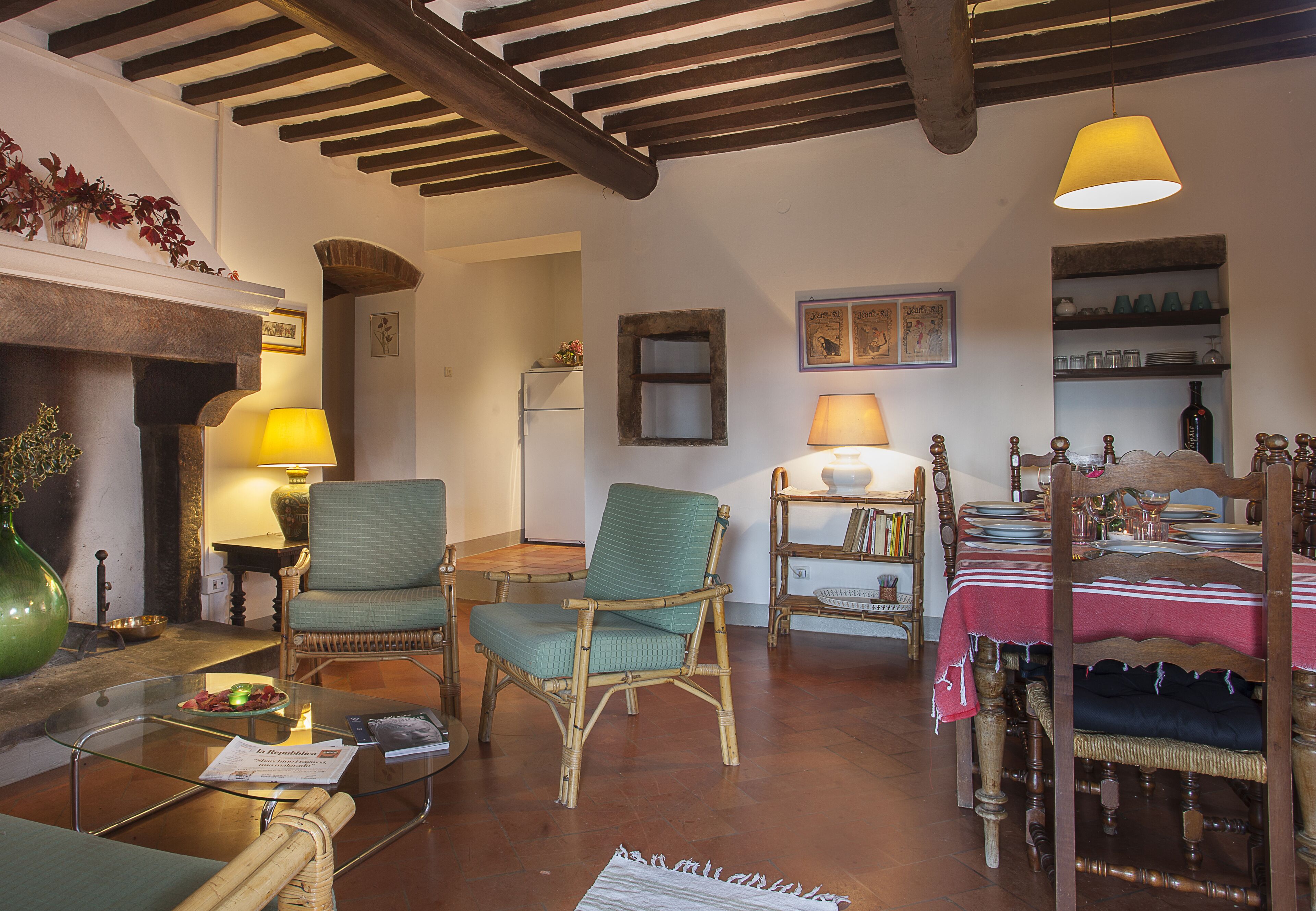 Un salon chaleureux avec une cheminée, des fauteuils confortables et un coin repas avec une table mise pour deux personnes.