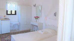 A bedroom with a bed, a bedside table, a desk, a chair, a mirror, and a window with curtains.
